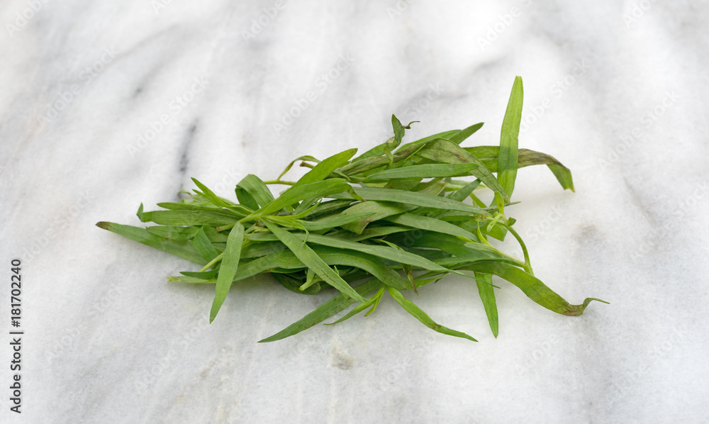 A small pile of organic tarragon leaves on a gray marble cutting board.