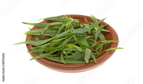 A small red clay bowl filled with organic tarragon leaves isolated on a white background.