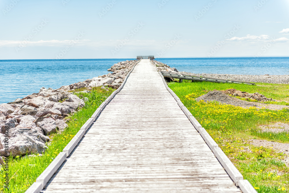 Empty long wooden boardwalk with nobody on pier dock quay with gulf of Saint Lawrence river in Gaspesie region of Quebec, Canada with converging lines