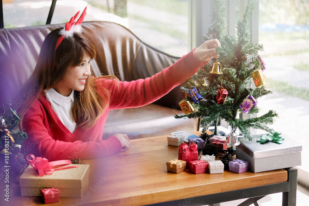Asian Woman wearing red sweater holding gold ornament and decorating Christmas tree at home. Asian Woman wearing red sweater holding gold ornament and decorating Christmas tree at home.