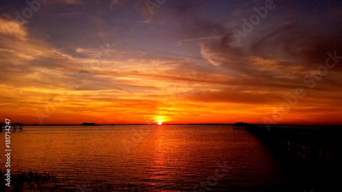 Beautiful orange sunset sky with sun setting along the horizon over water with scattered cloudscape and reflection on the water