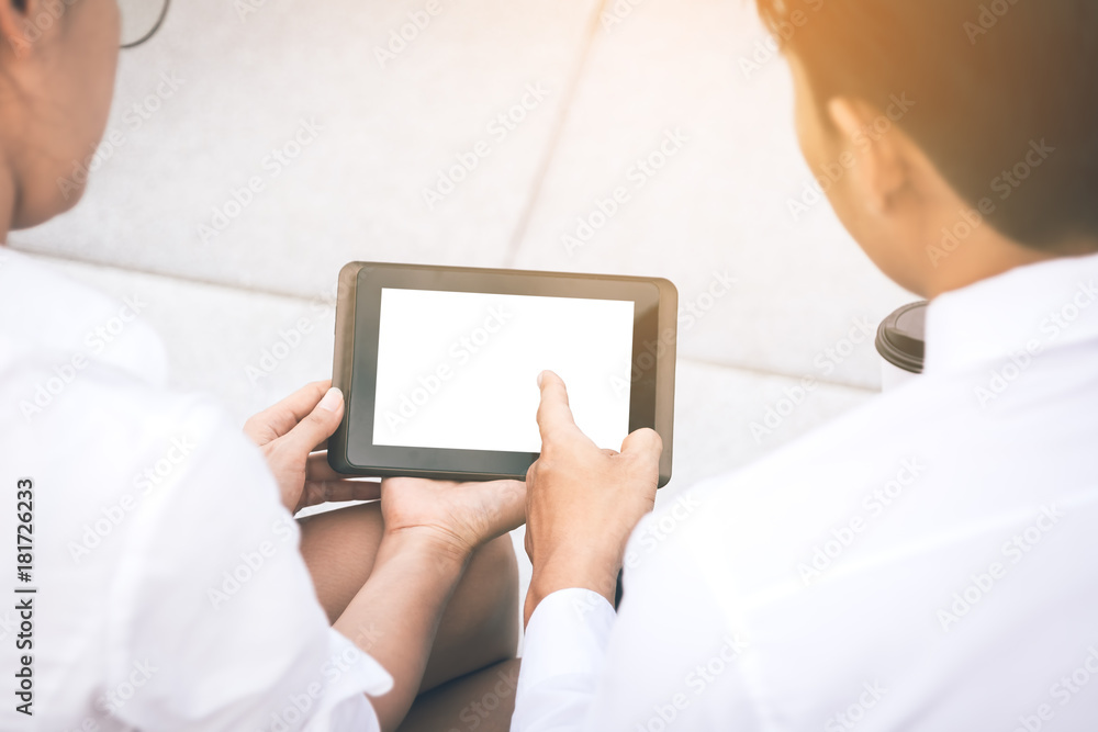Two business people holding digital tablet and pointing on blank screen with serious expression.