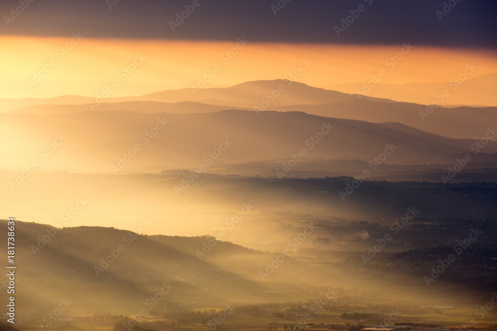 Sun rays coming out behind some mountains and hills at sunset