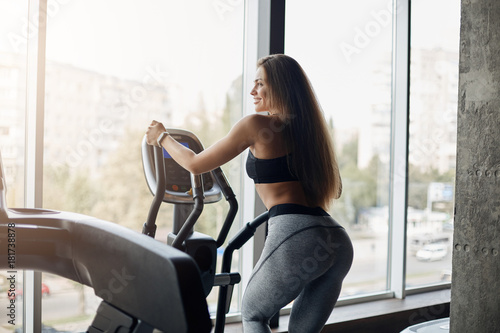 Young female body fitness coach using elliptical cross trainer to warm up before a long hard day at work early in the morning. Training buttocks.