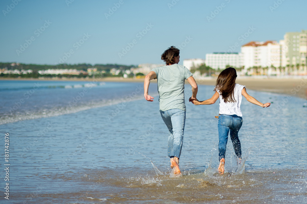 Man and woman running barefoot through the water.