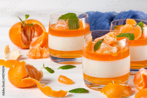 Creamy panna cotta with orange jelly in beautiful glasses, fresh ripe mandarin, blue textile on white wooden background. Delicious Italian dessert. Closeup photography.Selective focus.