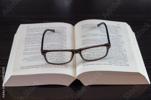  Thick book unfolded in the middle of the dark glasses framed on it isolated on black background 