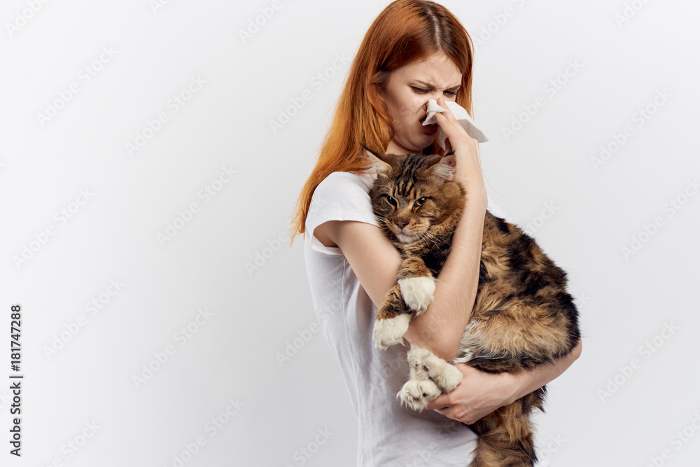 Young beautiful woman on a light background holds a cat, an allergy