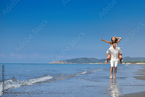 A guy carrying a girl on his back, at the beach, outdoors