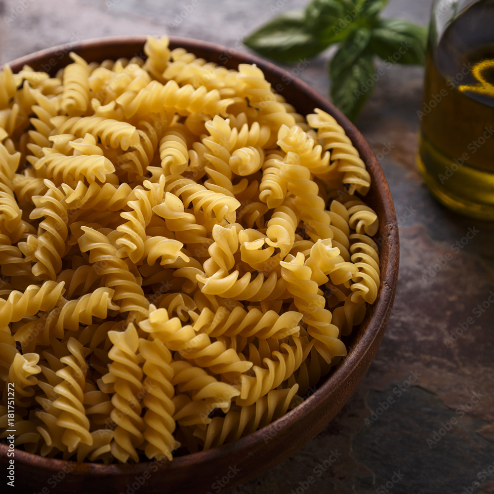 Fusilli Raw Pasta in a Wooden Bowl. With Olive Oil And Basil. Close-up. Fusilli Raw Pasta in a Wooden Bowl. With Olive Oil And Basil. Close-up.