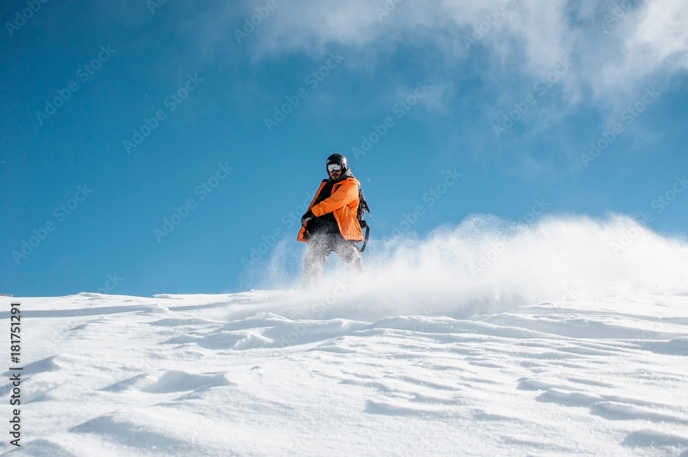 Snowboarder in orange sportswear riding down the powder snow hill