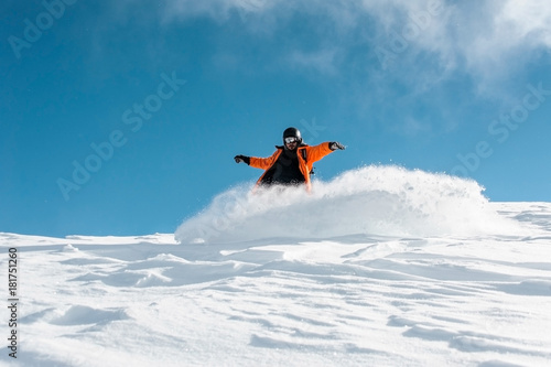 Male snowboarder in bright orange sportswear riding down the powder snow hill