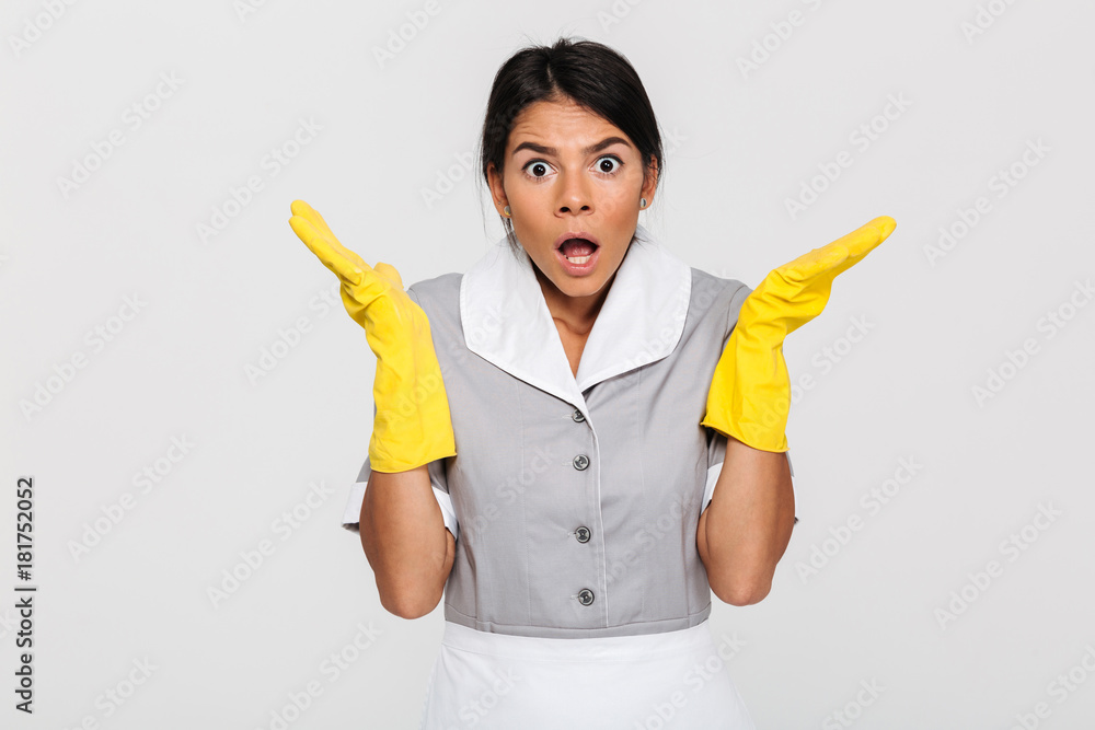 Close-up photo of amazed young female housekeeper in uniform and protective gloves standing with opened palms and looking at camera Close-up photo of amazed young female housekeeper in uniform and protective gloves standing with opened palms and looking at camera