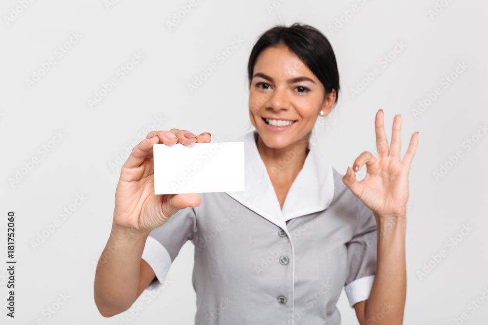 Portrait of happy maid in uniform showing empty sign card and OK gesture while standing and looking at camera Portrait of happy maid in uniform showing empty sign card and OK gesture while standing and looking at camera