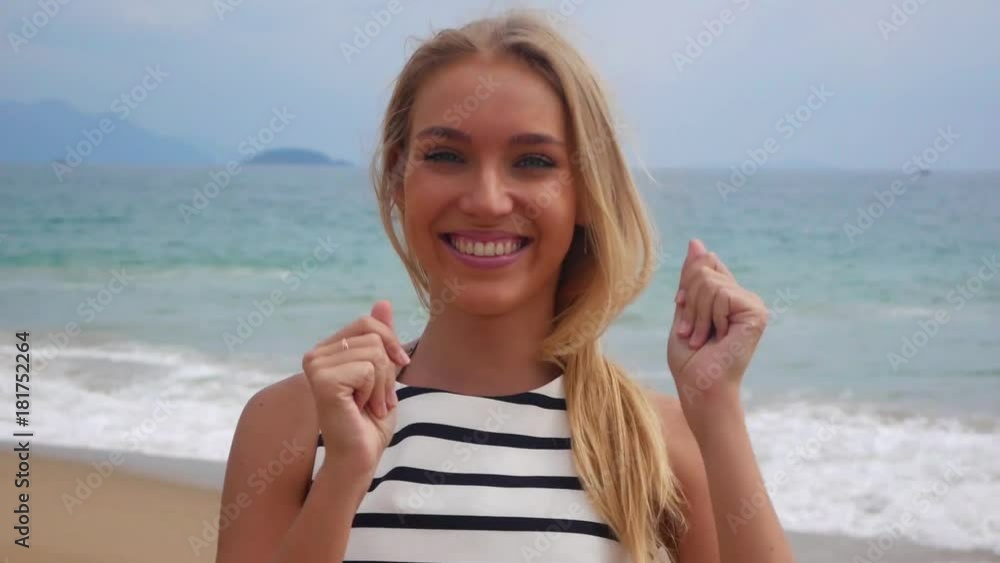 Closeup of a cheerful young beautiful girl smiling and raising her hands up against a background of storm on the sea Closeup of a cheerful young beautiful girl smiling and raising her hands up against a background of storm on the sea