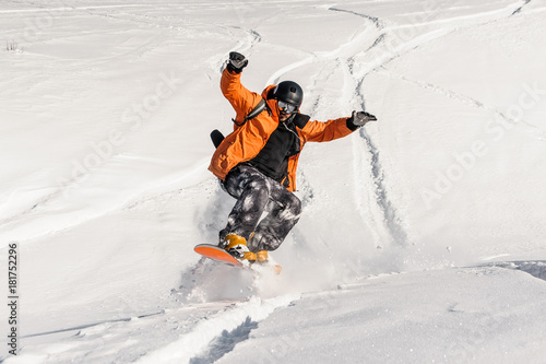 Young male snowboarder in orange sportswear jumping on the snow slope