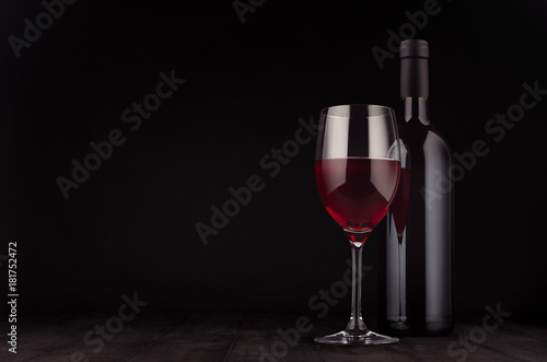Bottle of red wine and wine glass mock up on elegant dark black wooden background, copy space.