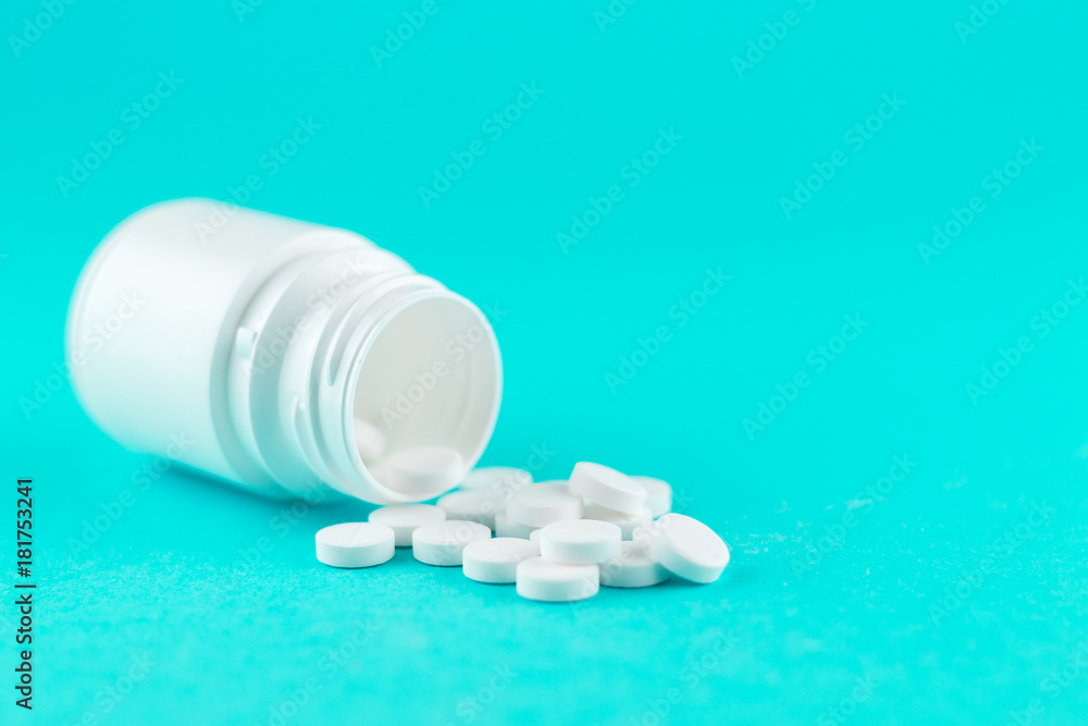Close up white pill bottle with spilled out pills on turquoise background with copy space. Focus on foreground, soft bokeh. Pharmacy drugstore concept Close up white pill bottle with spilled out pills on turquoise background with copy space. Focus on foreground, soft bokeh. Pharmacy drugstore concept