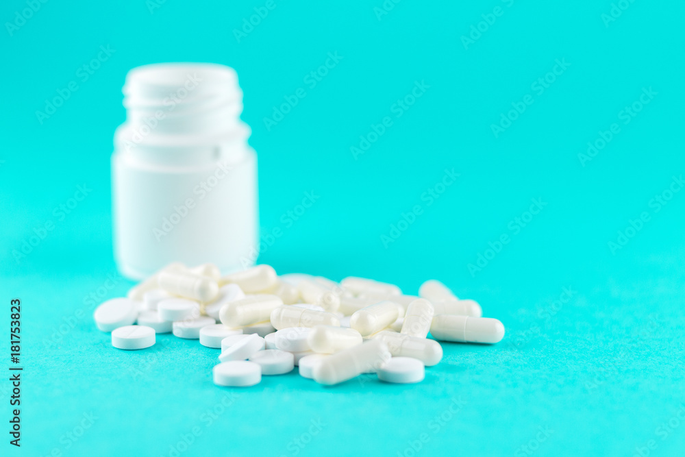 Close up white pill bottle with spilled out pills and capsules on turquoise background with copy space. Focus on foreground, soft bokeh. Pharmacy drugstore concept Close up white pill bottle with spilled out pills and capsules on turquoise background with copy space. Focus on foreground, soft bokeh. Pharmacy drugstore concept