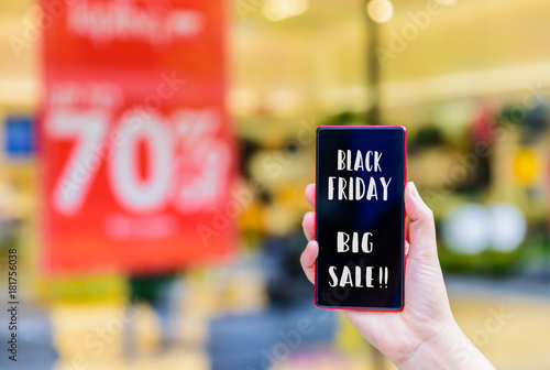 Hand holding mobile phone and black friday text with shopping mall background.