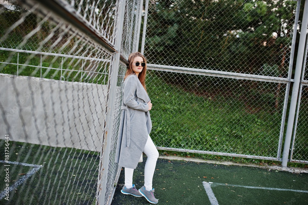 Girl in gray coat with sunglasses at small street stadium.