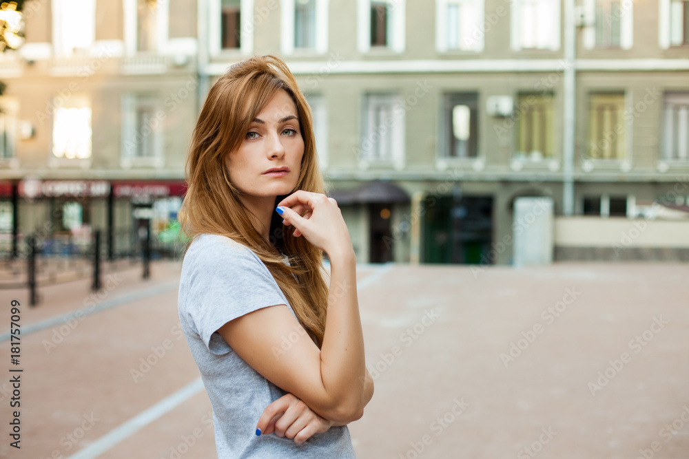 young thoughtfull redhead woman in a gray shirt walking around city. Concept of modern freedom hipster human