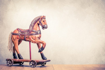 Vintage old antique Christmas wooden horse toy on wheels front concrete wall background. Holiday greeting card concept. Retro instagram style filtered photo