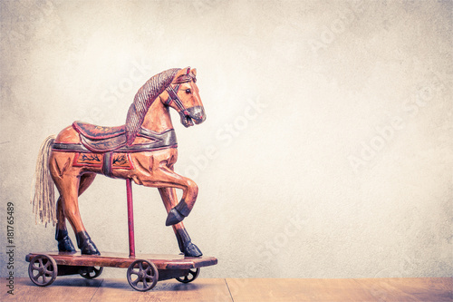Vintage old antique Christmas wooden horse toy on wheels front concrete wall background. Holiday greeting card concept. Retro instagram style filtered photo