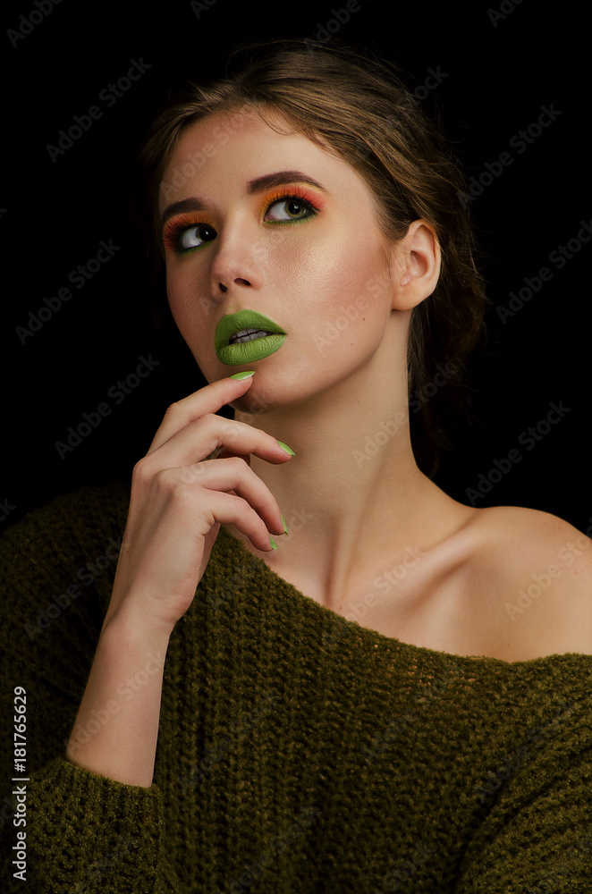 Bright colorful makeup in vivid colors on young attractive womens face. Beauty, portrait with orange eyeshadows and green lips. Sensual posing with hands. Cosmetics, healthy skin.