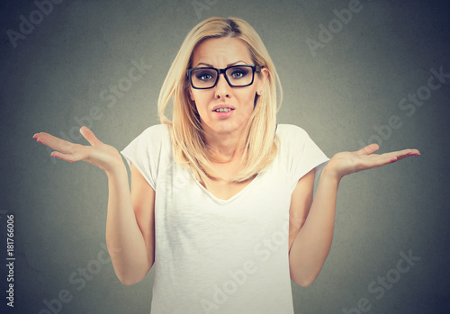 Portrait dumb looking woman arms out shrugs shoulders I don't know isolated on gray background. Negative emotion body language