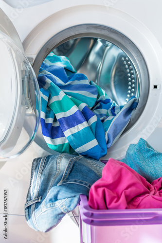 Blue and purple cotton clothes and linen in laundry basket and inside an open washing machine. Vertical.