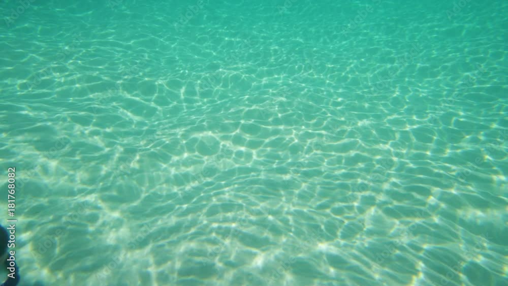 Shot in slow motion, a man underwater swims across the camera shot. The man is swimming under a beautiful turquoise water. Shot in slow motion, a man underwater swims across the camera shot. The man is swimming under a beautiful turquoise water.