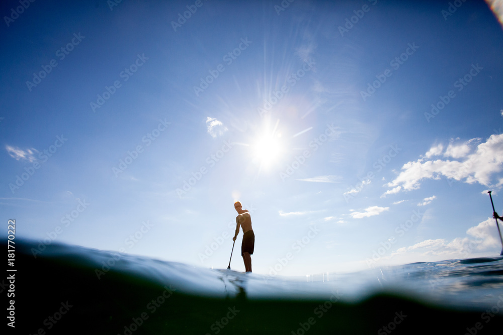 Young man paddle boarding, surface level view Young man paddle boarding, surface level view