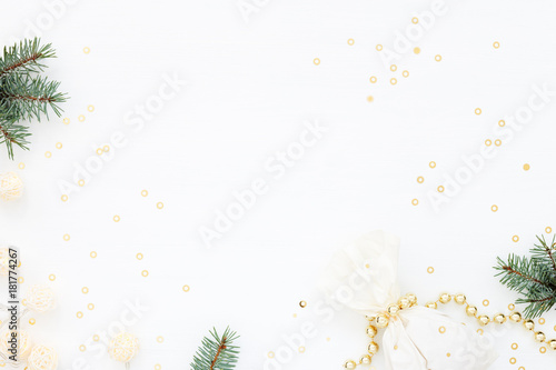 Bright Christmas composition with a gift & New Year decoration. Gold pearl beads, fir, paper bag, garland and confetti on white. Flat lay. Winter holiday card