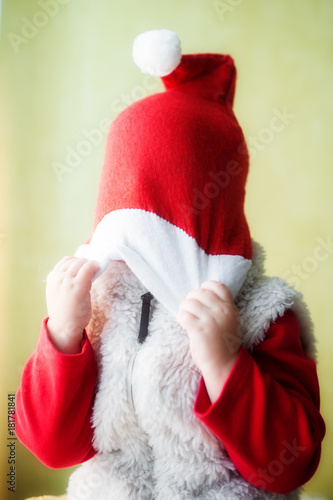 The kid pulls a red Santa Claus cap over his head. The face is not visible.