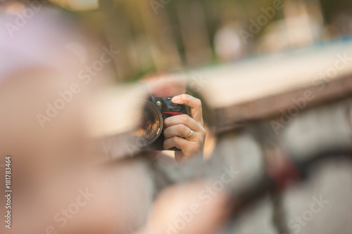 Reflection in a small circular mirror of a photographer with a camera. A hand with a gold ring that holds the camera is visible. Selective focus.