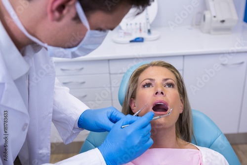 Dentist holding tools while examining woman at medical clinic