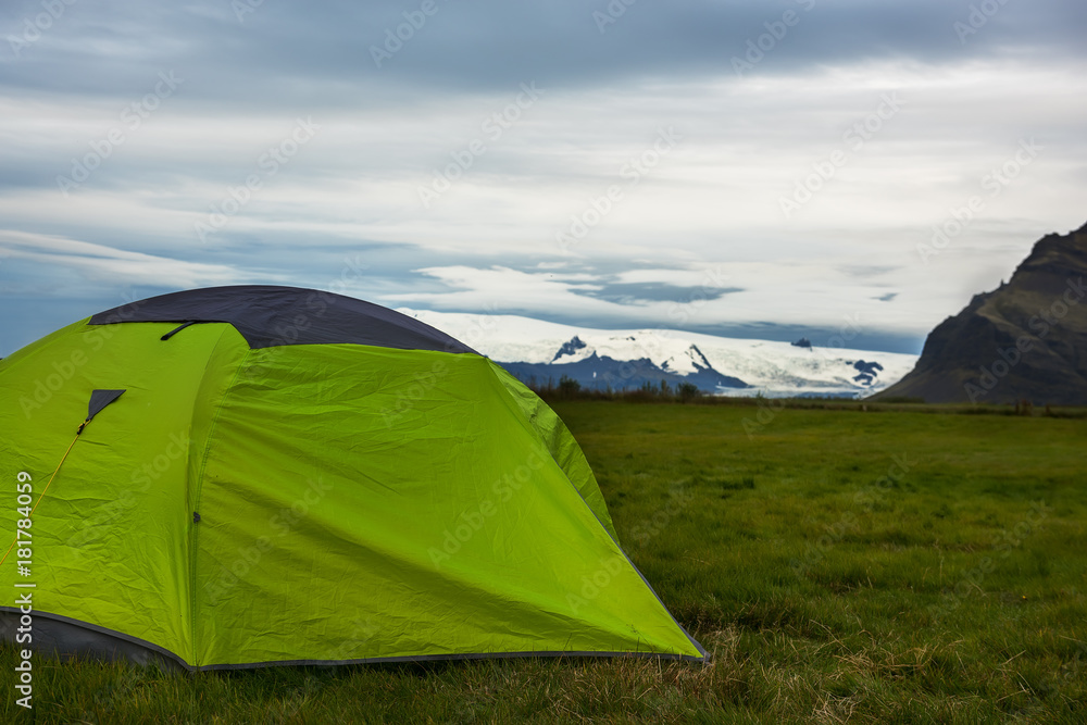 tourist tent on a glade with green grass. In the background are snow-capped mountains. Iceland.
