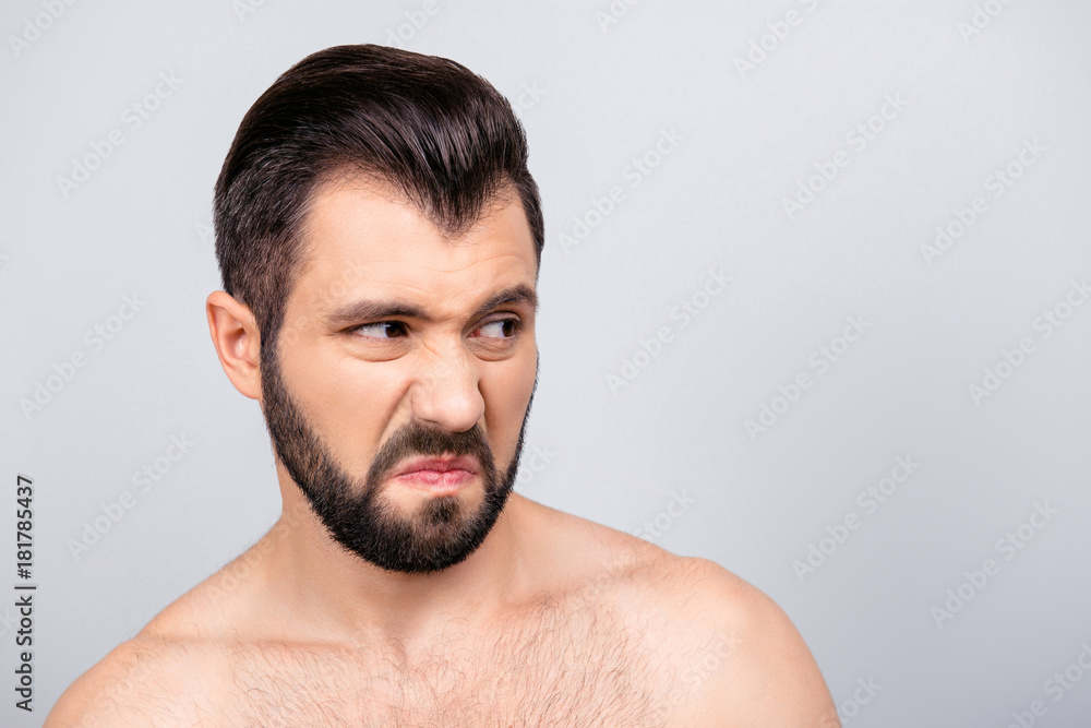 Close up portrait of emotional man with dislike emotion on his face, looking to the side, standing over grey background Close up portrait of emotional man with dislike emotion on his face, looking to the side, standing over grey background