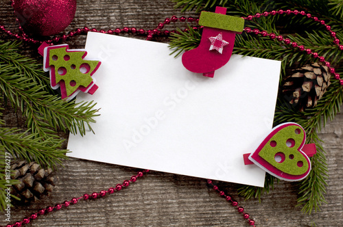 Christmas background with white paper. Christmas card with clean sheets the attached decorative clothespegs to fir-tree branches on a wooden background. 