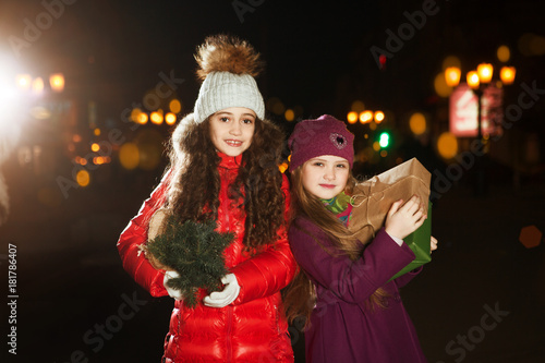 beauty two little girls with christmas gift and Christmas tree in city in the evening. Christmas time. Happy Christmas holidays! 