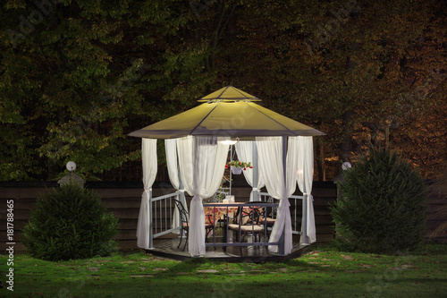 A beautiful gazebo with a table in the evening, autumn park is lit by a lamp. photo