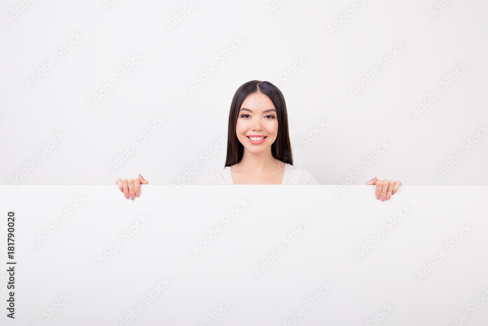 Copy space portrait of charming, attractive, cute girl hiding, standing behind empty white horizontal wall isolated over white background Copy space portrait of charming, attractive, cute girl hiding, standing behind empty white horizontal wall isolated over white background