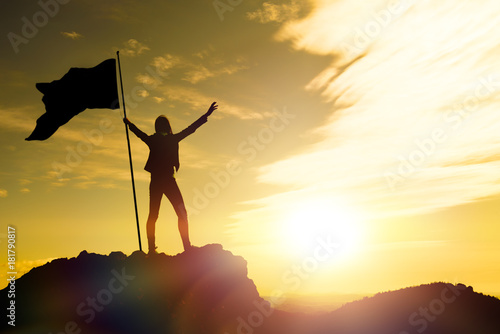 High achievement, silhouettes of the girl, flag of victory on the top of the mountain, hands up. A man on top of a mountain. Conceptual design. Against the dramatic sky with clouds at sunset. photo