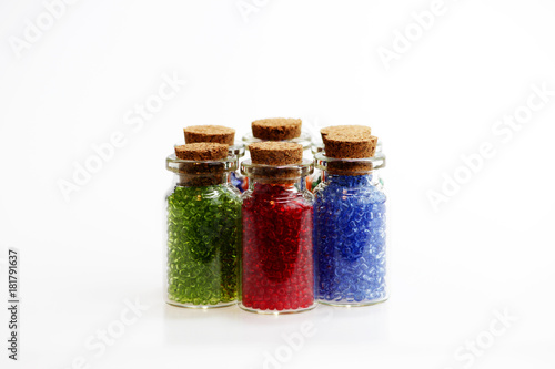 Six tiny glass bottles with a cork stopper, filled with a rainbow colours of beads, on a white background. photo