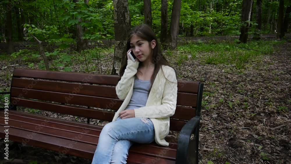 Young attractive girl speak to phone on bench. Summer park. Smile. HD video footage shooting static camera. Young attractive girl speak to phone on bench. Summer park. Smile. HD video footage shooting static camera.