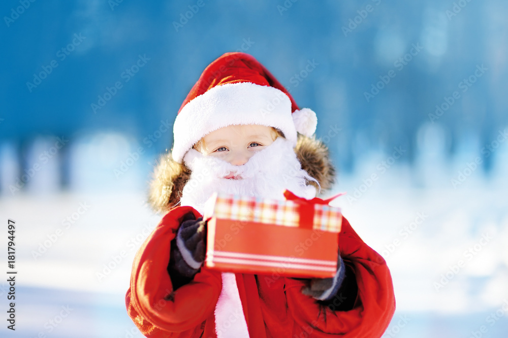 Obraz premium Funny little boy wearing Santa Claus costume in winter snowy park