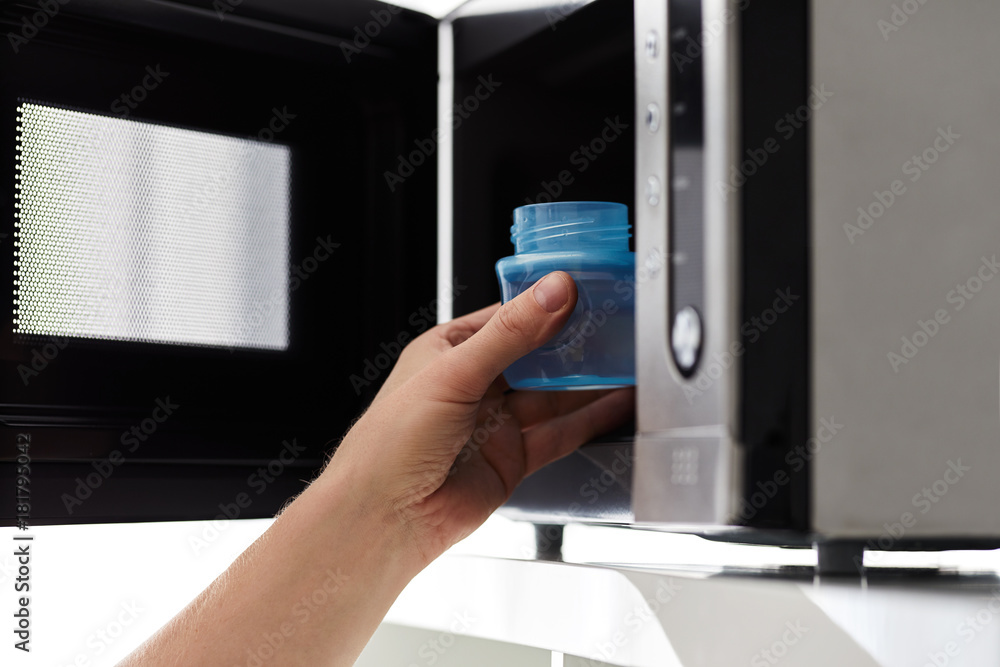 Father putting a baby bottle with water into a microwave Father putting a baby bottle with water into a microwave