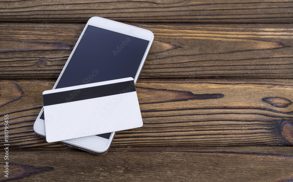 Phone and plastic card on wood table background. Conceptual presentation of payments or business activities via the Internet and mobile devices Phone and plastic card on wood table background. Conceptual presentation of payments or business activities via the Internet and mobile devices