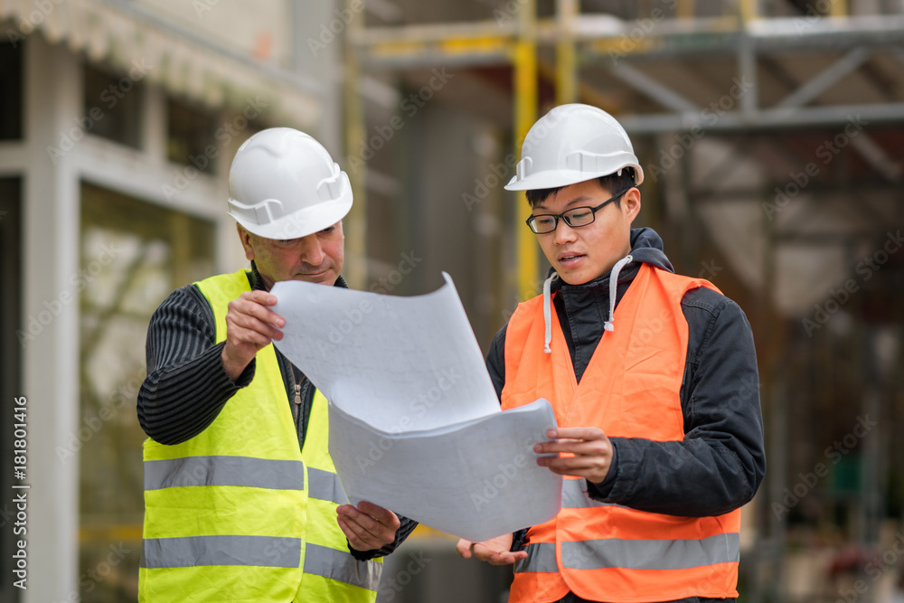 Young Asian apprentice at work on construction site with senior engineer. Outdoors Young Asian apprentice at work on construction site with senior engineer. Outdoors